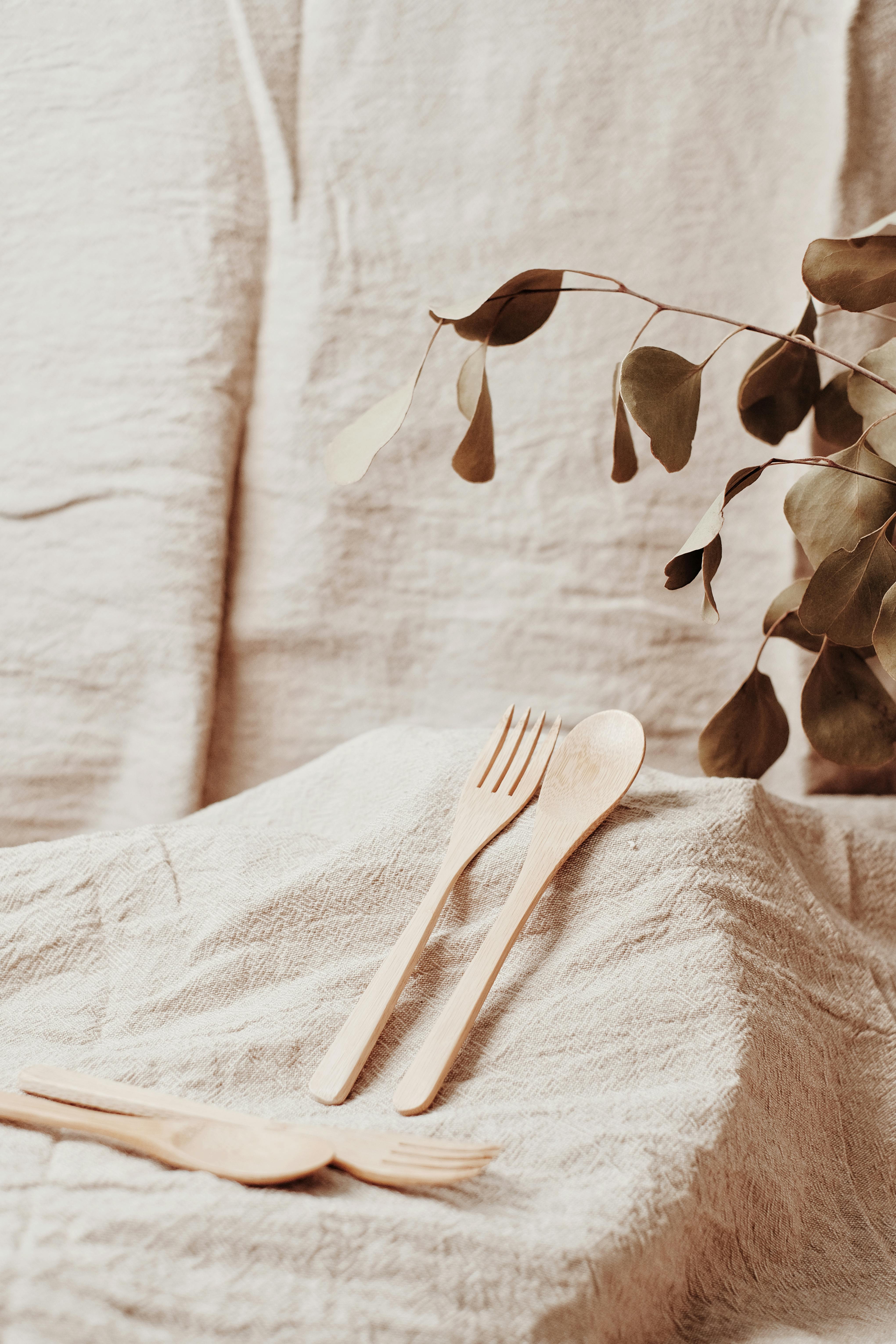 Sustainable wooden fork and spoon on rustic fabric with plant leaves, promoting zero waste living.