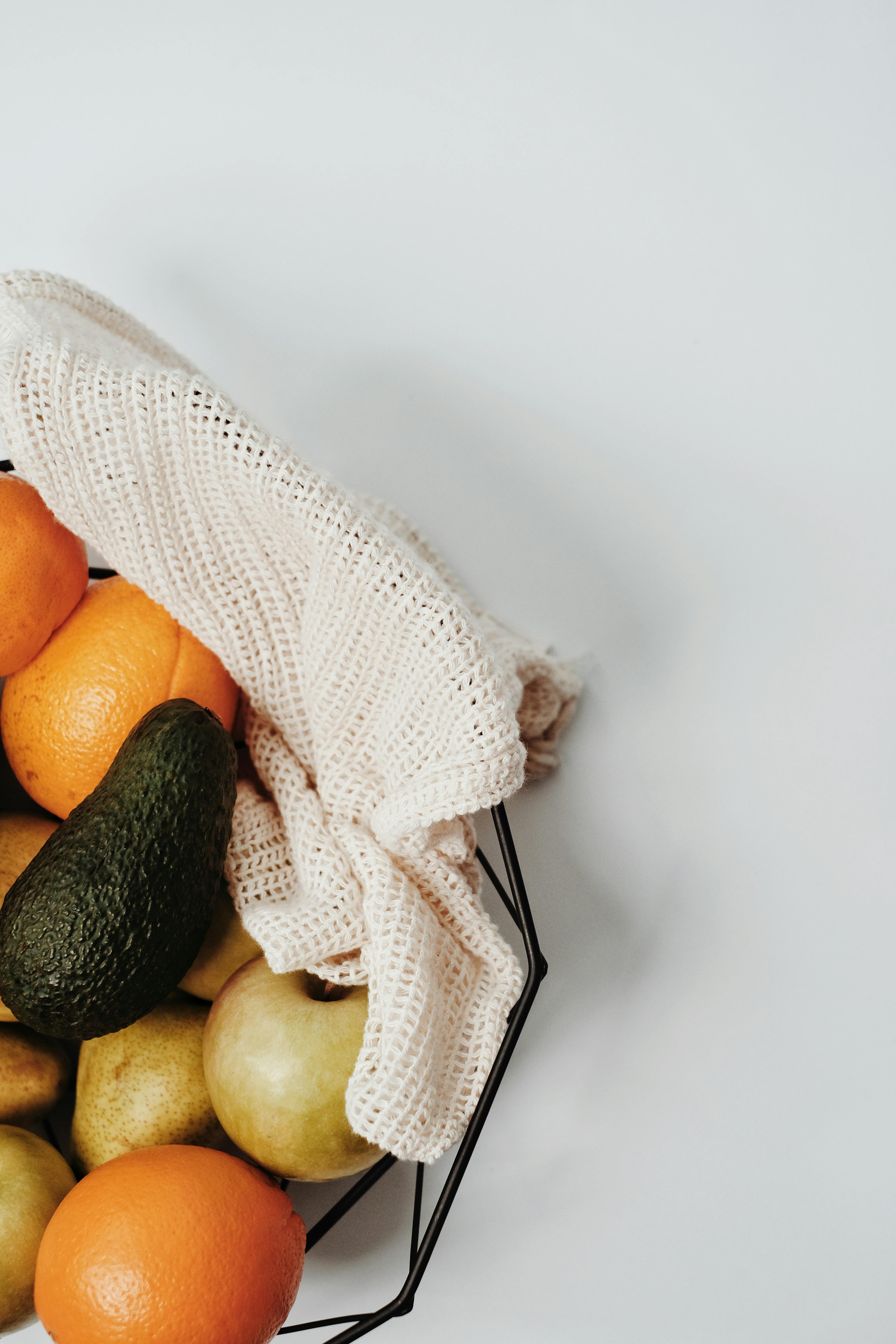 Aerial view of assorted fresh fruits in a reusable basket with a burlap cloth promoting sustainable shopping.