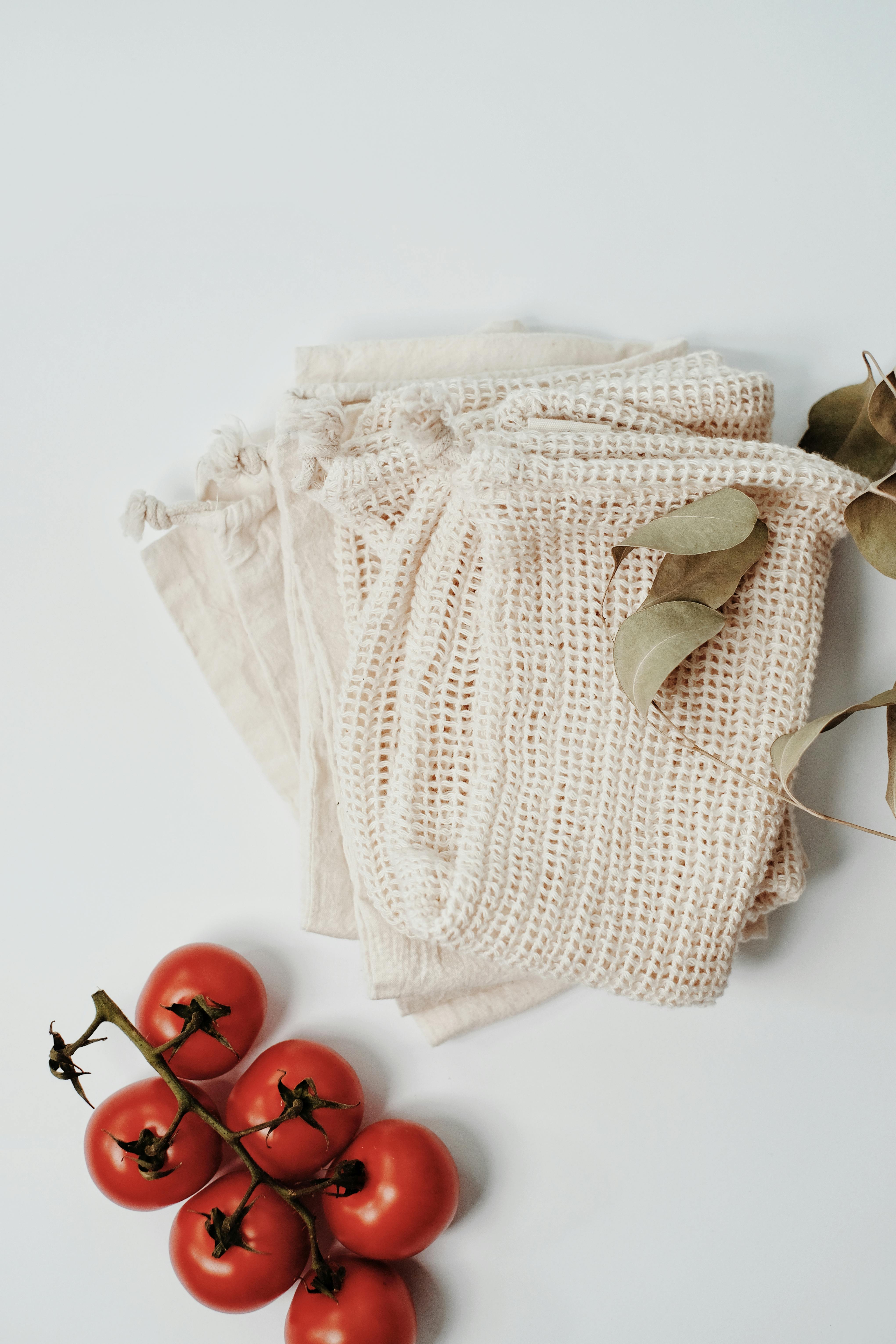 Overhead view of eco-friendly reusable bags with vine-ripened cherry tomatoes on a white surface.