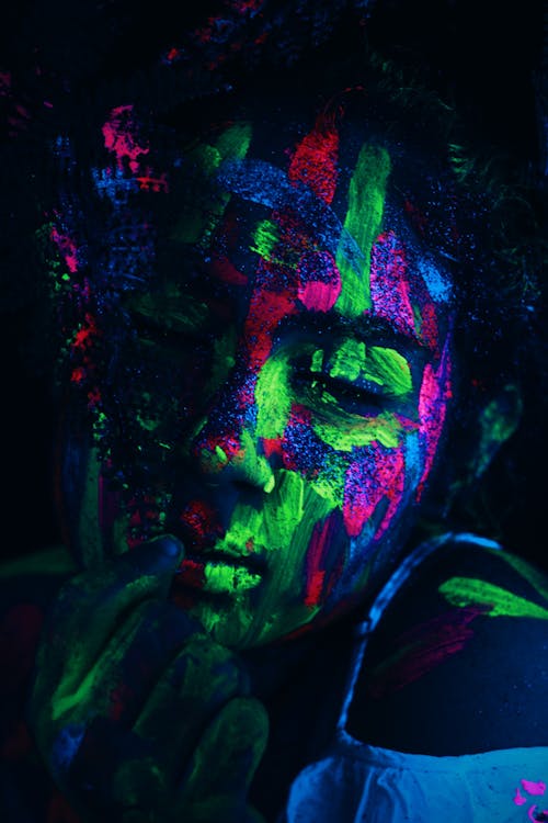 Woman covered with colorful neon paints shining on face under ultraviolet light in dark studio