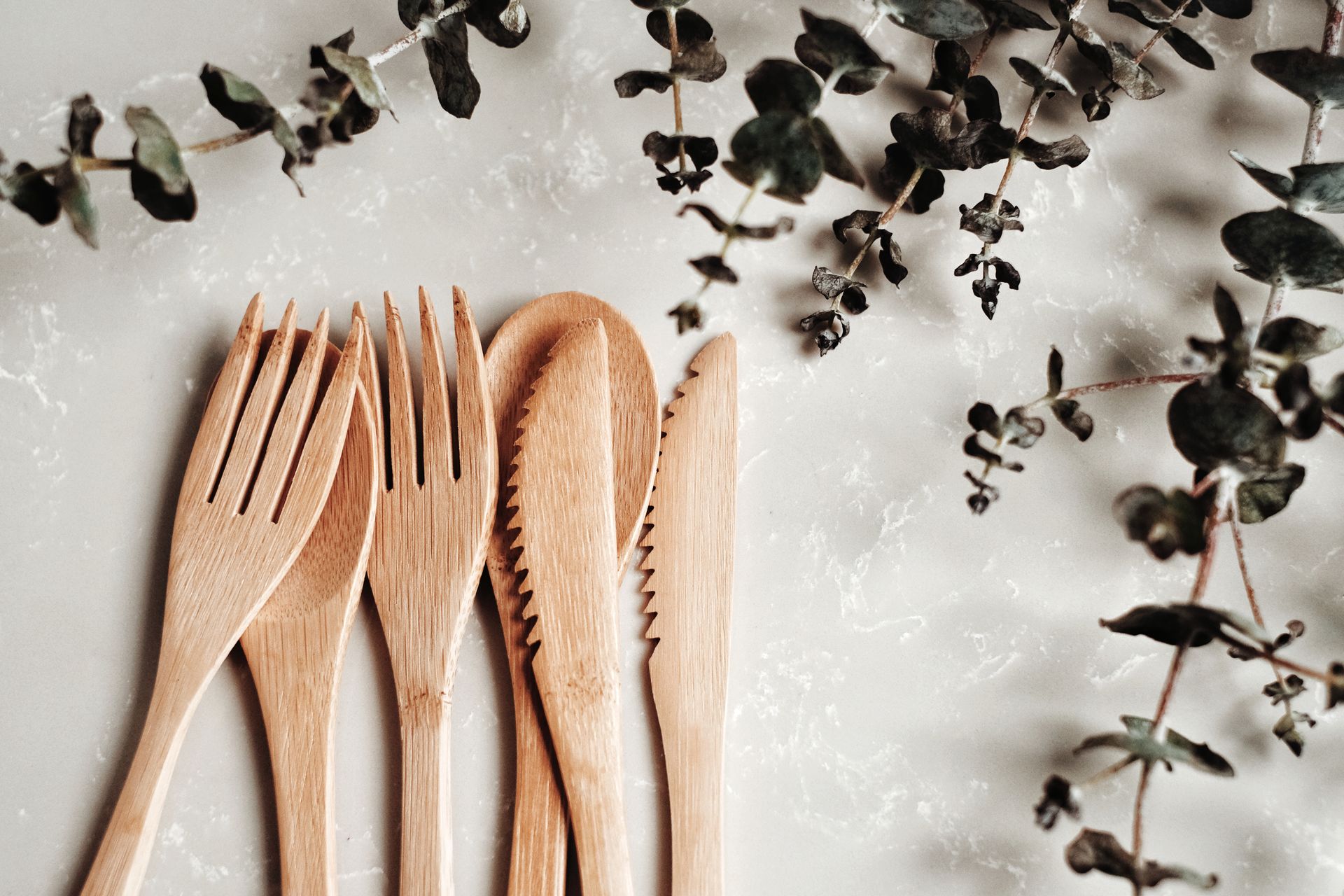 Close-up of bamboo utensils and eucalyptus branches on a marble surface, highlighting sustainability.