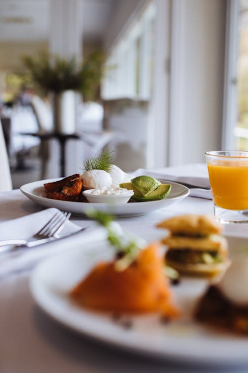 Fresh avocado slices with poached eggs and cheese sauce on plate near glass of refreshing beverage for brunch