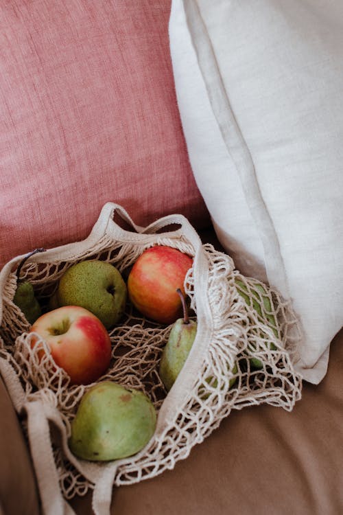 Free High angle net shopper bag with tasty green and red apples placed on pink comfy couch Stock Photo
