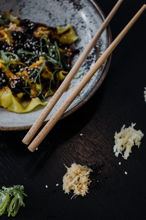 High angle of ceramic plate with palatable Asian food and wooden chopsticks placed on table in cafe