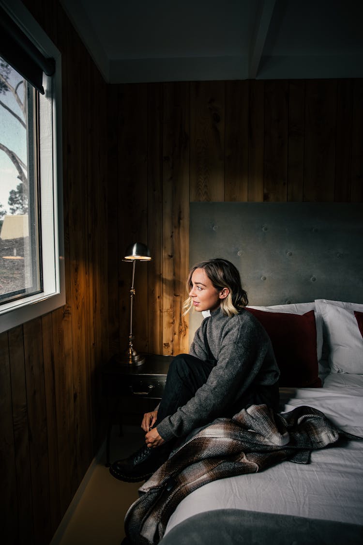 Thoughtful Woman On Bed Putting On Shoes