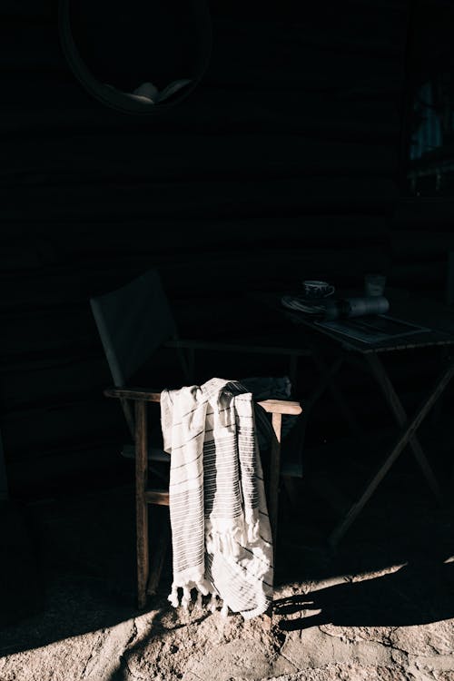 Free Comfy wooden chair with soft plaid placed near table with cup of hot drink in shade near house Stock Photo