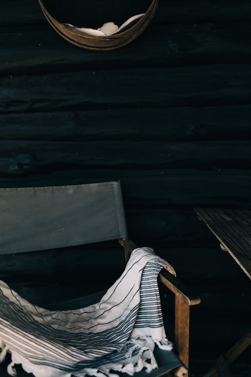 Free Empty comfortable chair with soft warm coverlet placed near wooden table on porch against wall of residential house Stock Photo