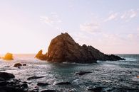 Wavy sea washing rocky formation under sundown sky