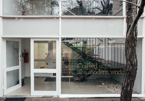 Modern building with inscription on windows and doorway and staircase located on street in city with tree trunk