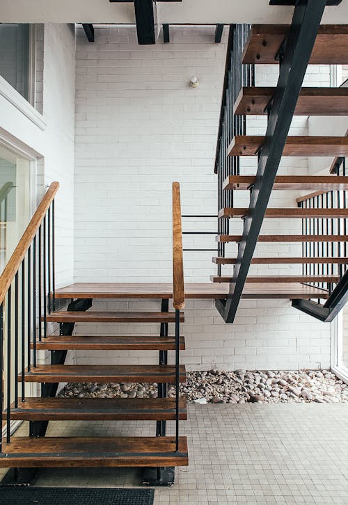 Black stairway with wooden railings of residential building placed on terrace with white brick wall of modern house