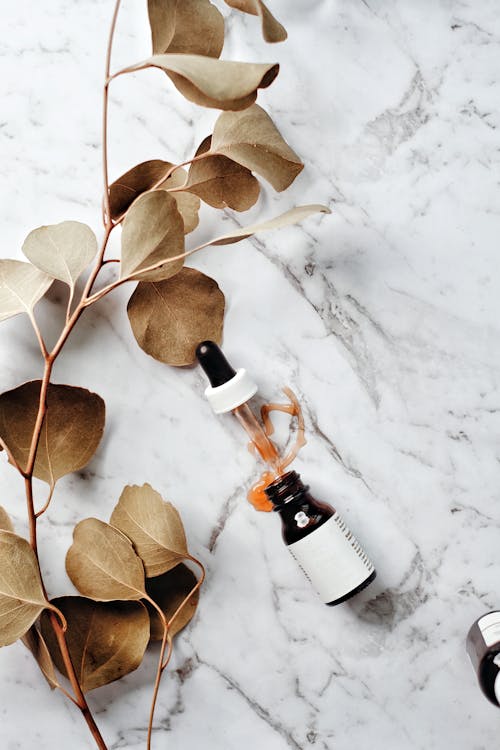 Free A Glass Bottle with Serum and Pipette Lying on a Marble Surface with an Eucalyptus Twig  Stock Photo