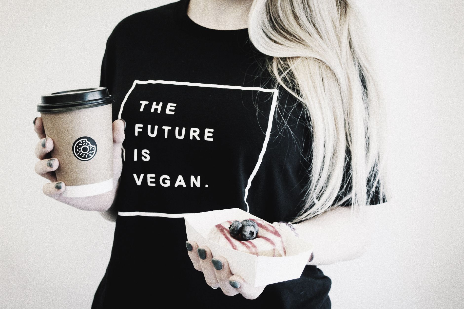 Person holding vegan coffee and donut, showcasing vegan lifestyle with a stylish touch.