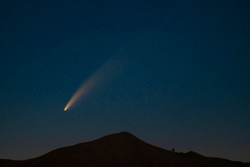 Free A breathtaking capture of a comet streaking across a star-filled night sky above a mountain silhouette. Stock Photo