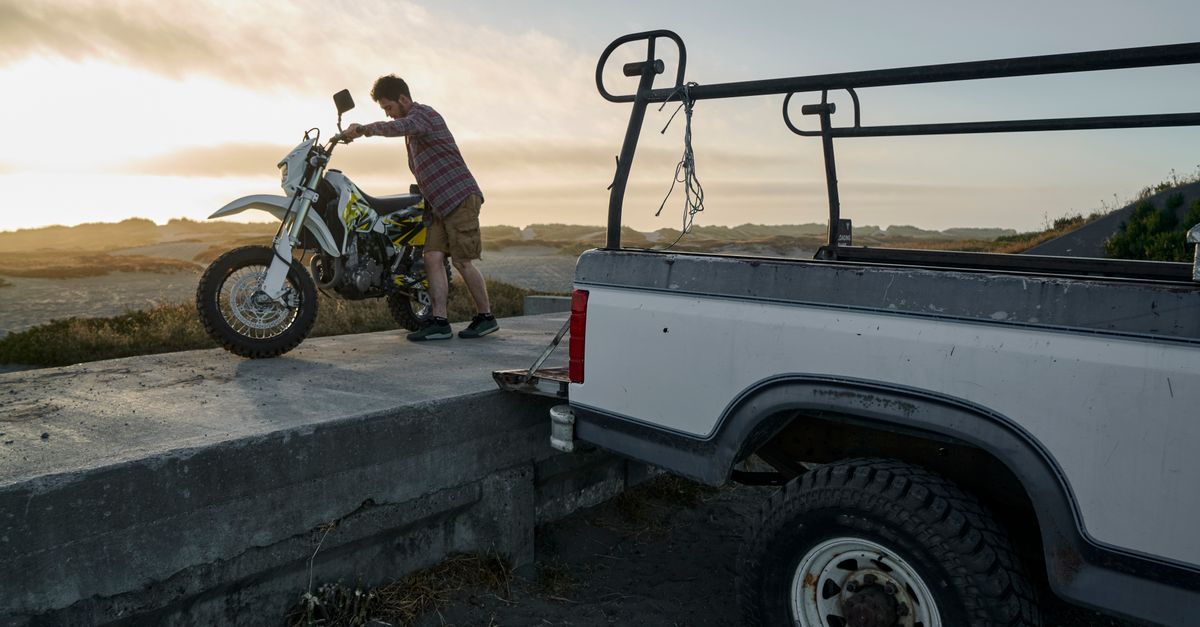 A man unloads a motorcycle from a truck at sunset, showcasing adventure and freedom.
