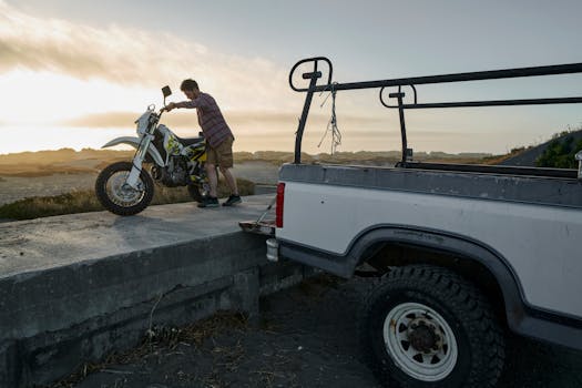 A man unloads a motorcycle from a truck at sunset, showcasing adventure and freedom.