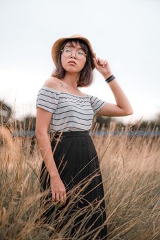 一位戴着眼镜和帽子、穿着时髦衣服的棕色短发年轻女性站在田野里