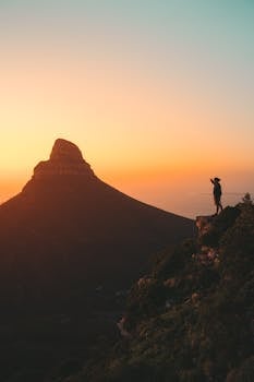 Silhouette of a hiker at sunset on Lion's Head, Cape Town. Stunning orange sky and rugged terrain.