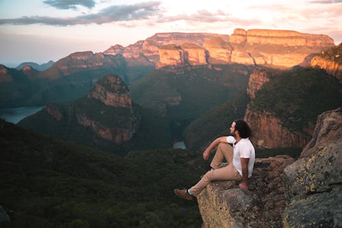 Free Woman in White Tank Top Sitting on Brown Rock Formation Stock Photo