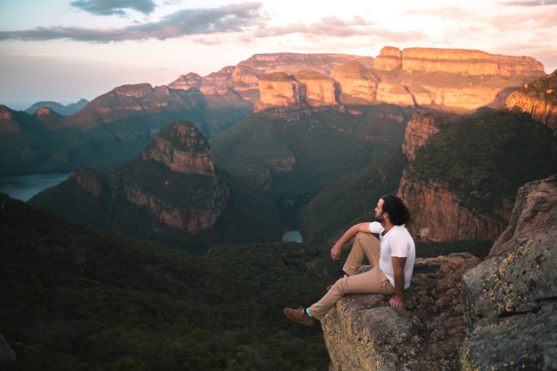 A man sits on a cliff enjoying a sunset view at Blyde River Canyon, capturing nature's beauty.