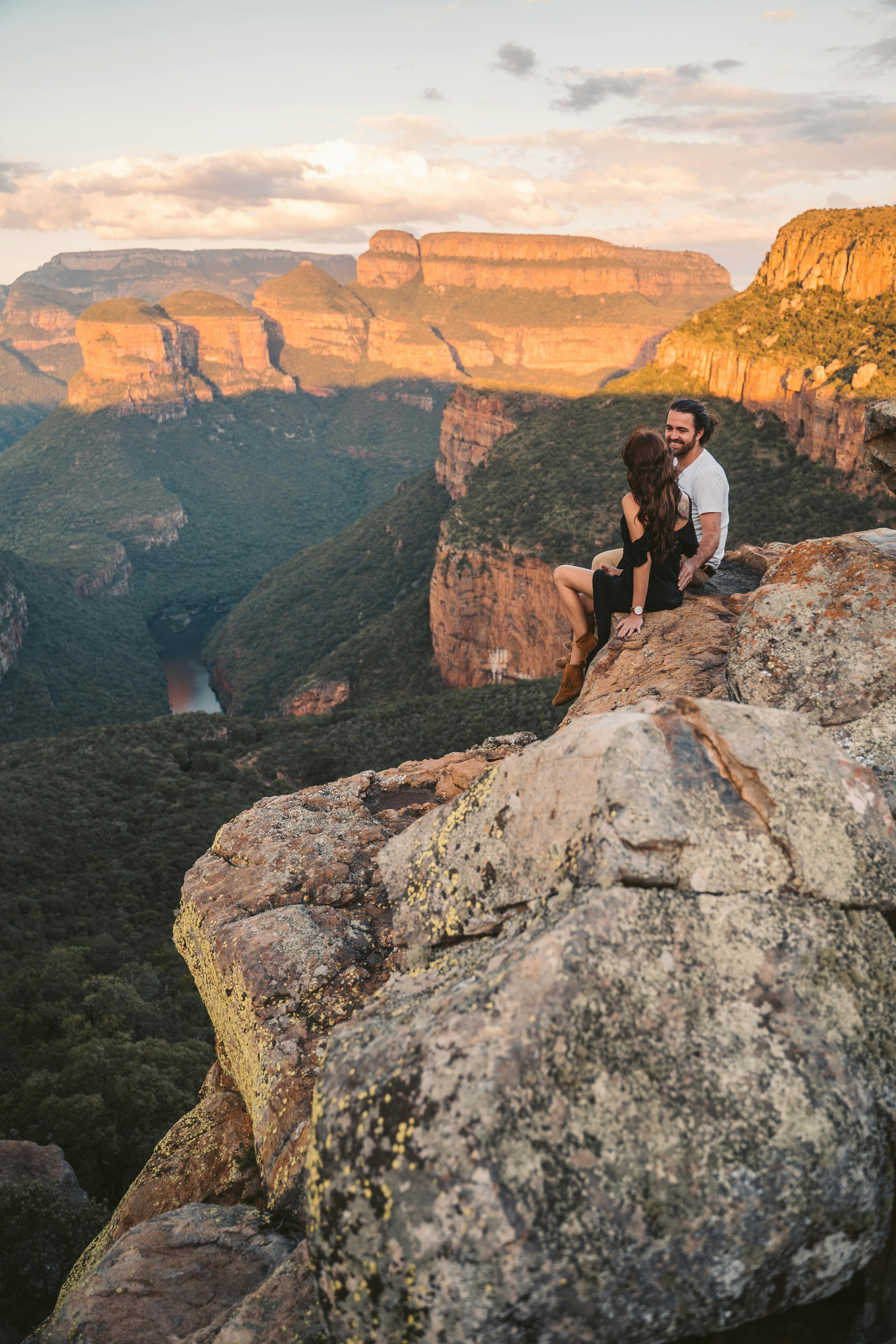在南非日落时分，夫妇坐在岩石悬崖上，俯瞰着令人惊叹的峡谷景色