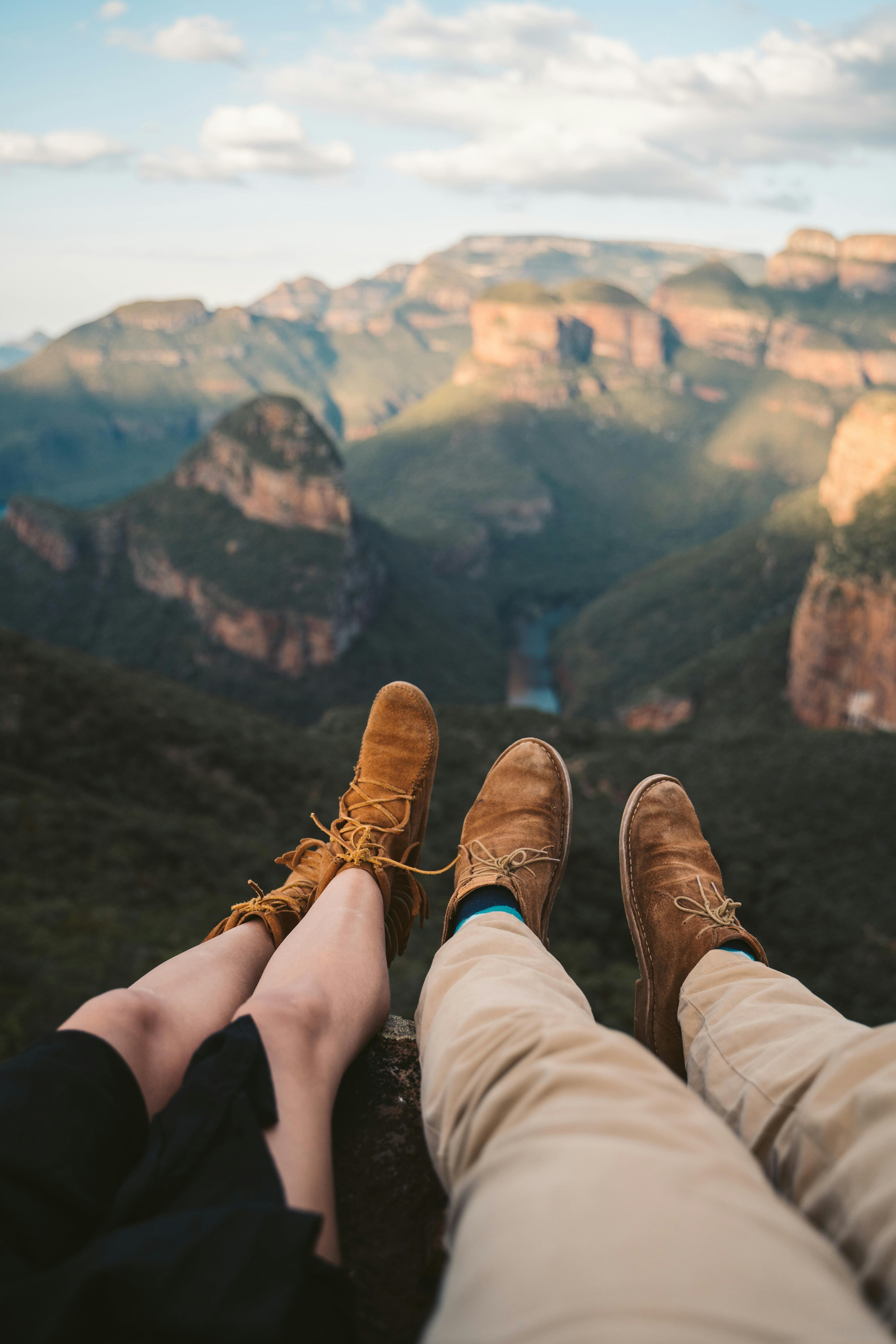 Free Relaxing mountain view from a cliff with a couple's legs in view, capturing outdoor adventure. Stock Photo