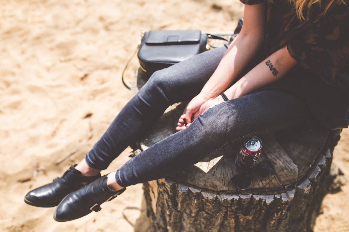 Free Person Wearing a Blue Denim Jeans and Black Leather Shoes Sitting on a Trunk Stock Photo