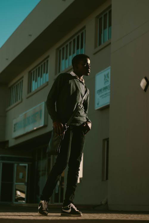 Free Serious black teen standing near building and thoughtfully looking away Stock Photo