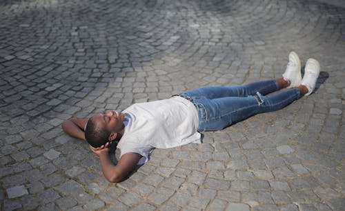 Man in White Shirt and Blue Denim Jeans Lying on Concrete Floor