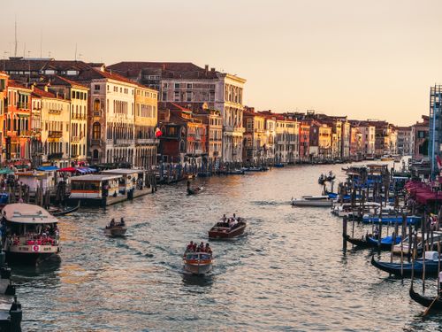 Free Explore the vibrant life of Venice's Grand Canal with boats and historical architecture illuminated by sunset tones. Stock Photo