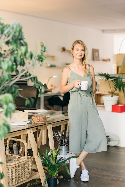 Free Woman in a Green Jumpsuit Holding a White Mug Stock Photo