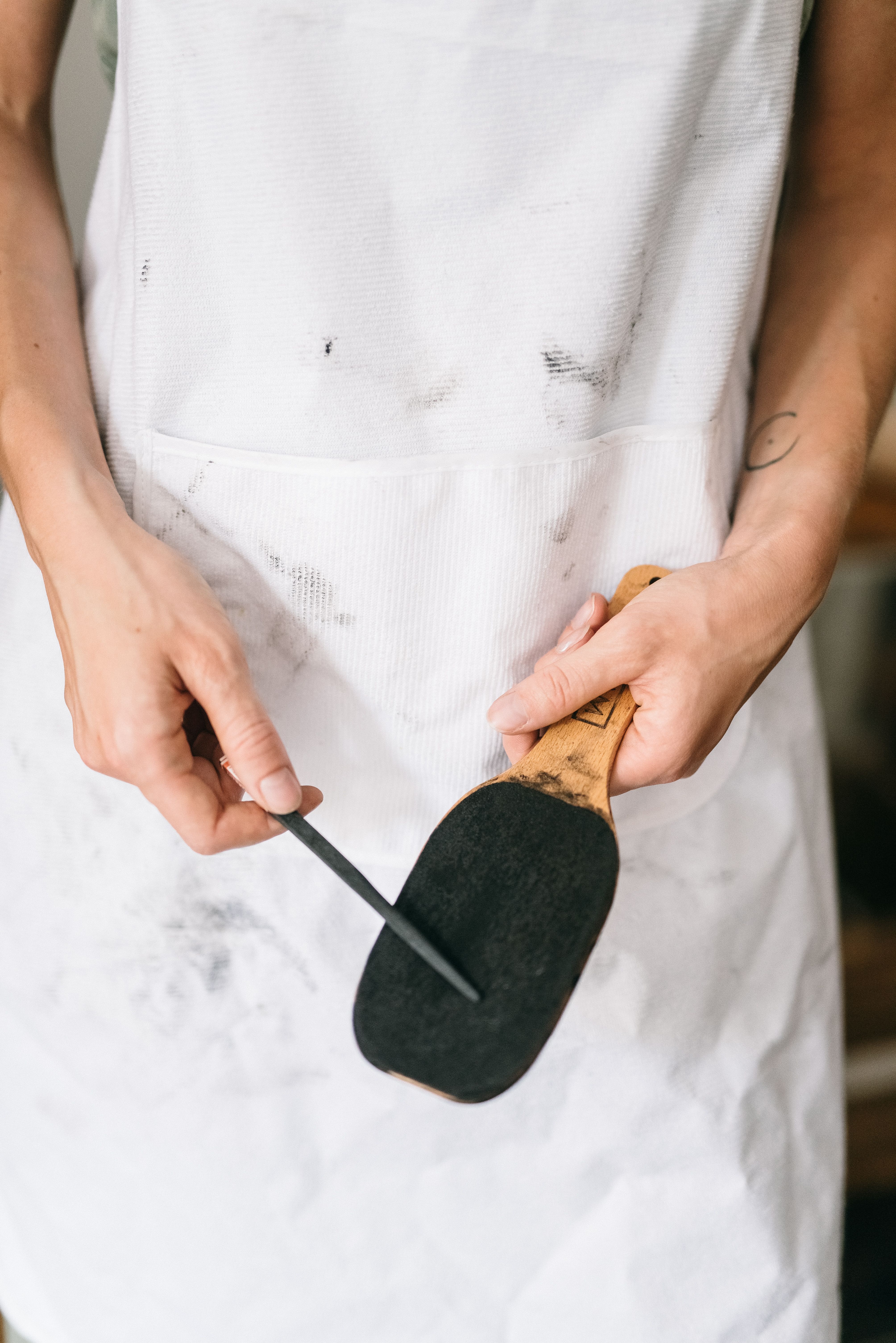Close-up of artist sharpening charcoal tool on a white apron, showcasing creativity and art preparation.