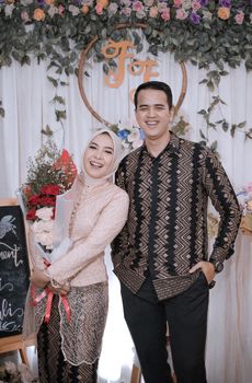 Smiling couple in traditional attire holding a bouquet at their engagement celebration. - Fotografer Sidoarjo
