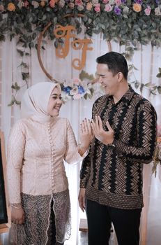 Smiling couple in traditional attire celebrating a joyous wedding moment indoors. - Fotografer Sidoarjo