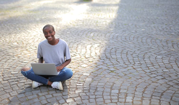 A Person Sitting On The Ground While Using A Laptop