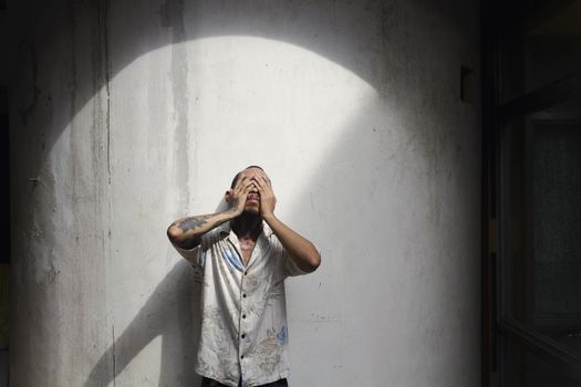 一名棕色短发、手臂上有纹身的年轻人，穿着衬衫站在白墙边，闭着眼睛