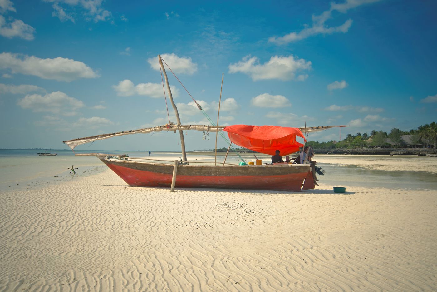 A traditional dhow with a red sail on a white-sand beach at Zanzibar, Tanzania