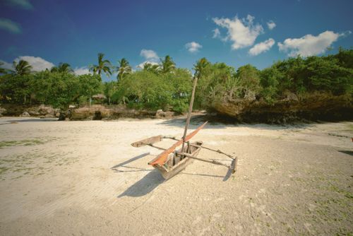 Free Traditional wooden canoe on a sandy beach in Zanzibar with lush greenery and clear blue sky. Stock Photo