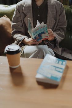 一名女子穿着西装外套，坐在咖啡馆舒适的沙发上看书