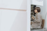 一名年轻女子穿着西装外套，坐在咖啡店的窗前看书