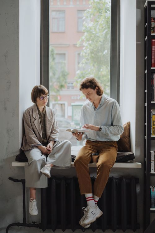 Free Two young adults enjoy a book in a cozy indoor setting by the window. Stock Photo