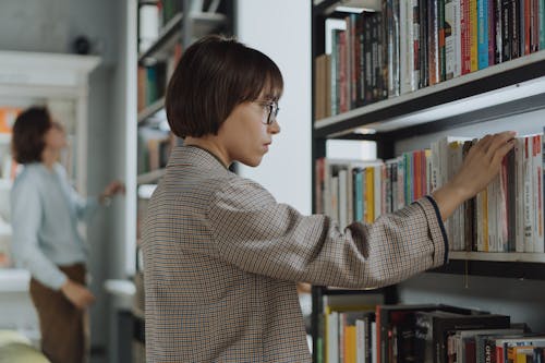 Woman in White and Brown Checkered Dress Shirt Standing in Front of Book Shelf