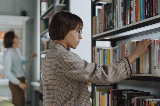 在现代图书馆里，一名穿着格子夹克的年轻女子正在浏览书籍