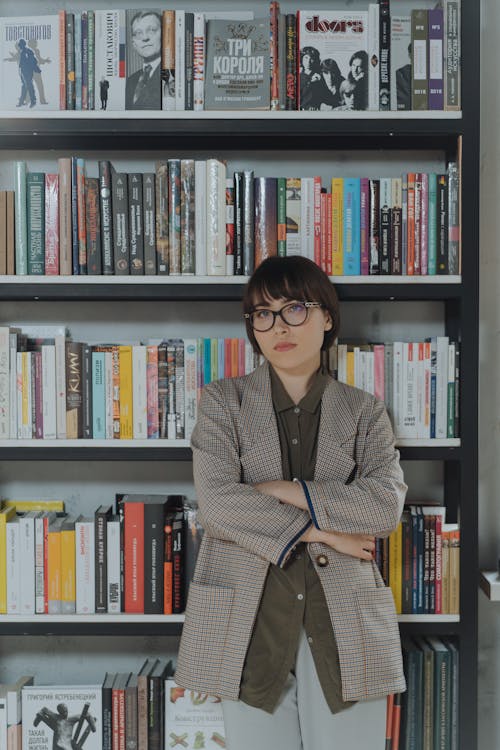 Woman in Gray Coat Standing Near Book Shelf