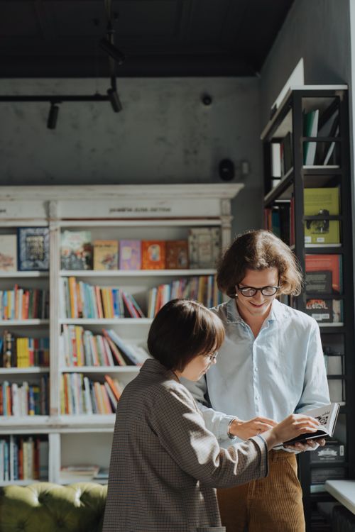 Free Two adults engage in a joyful book discussion in a cozy library setting. Stock Photo