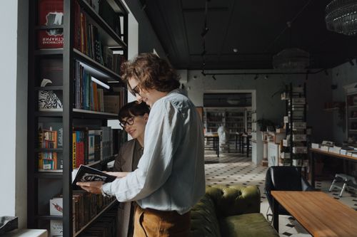 Free Two adults browsing books in a stylish library, sharing joy and knowledge. Stock Photo