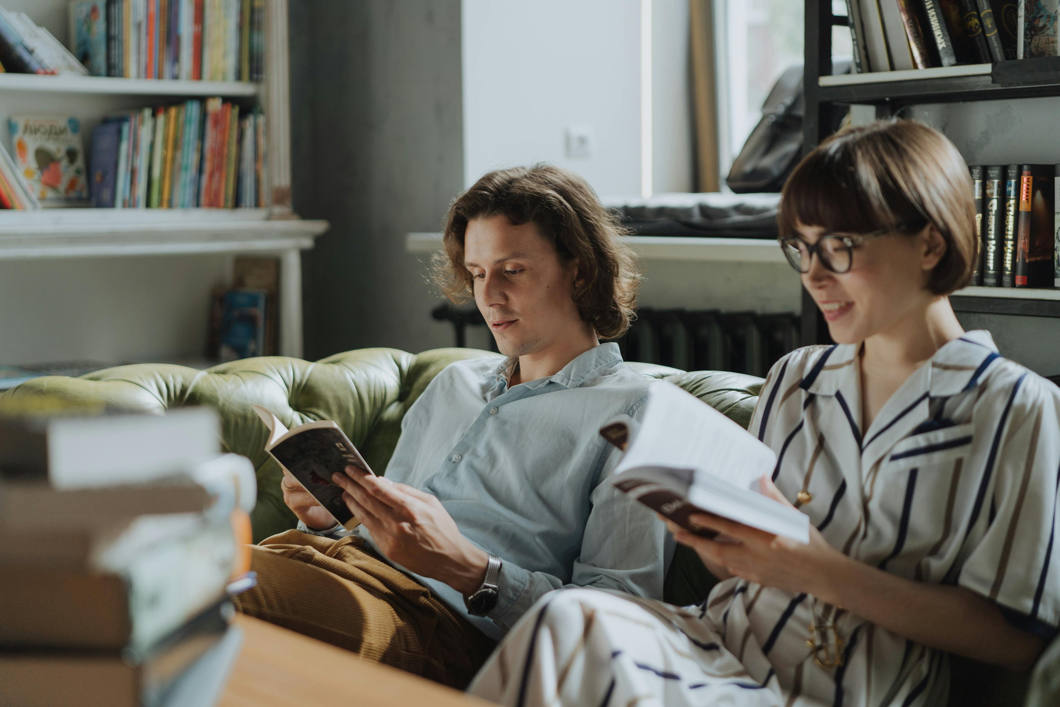 A man and woman relax on a couch reading in a cozy home library.