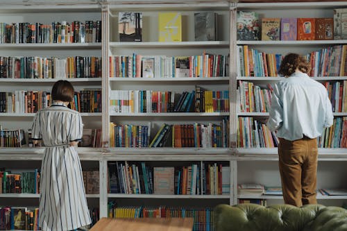 茶色の木製の本棚の横に立っている白いドレスシャツの男