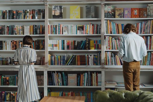 Man in White Dress Shirt Standing Beside Brown Wooden Book Shelf