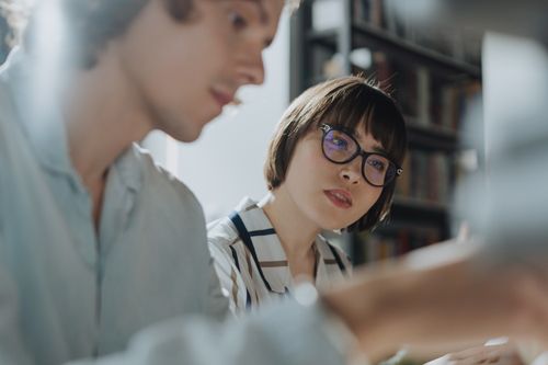 Free Two young adults in a library sharing ideas and discussing topics. Stock Photo
