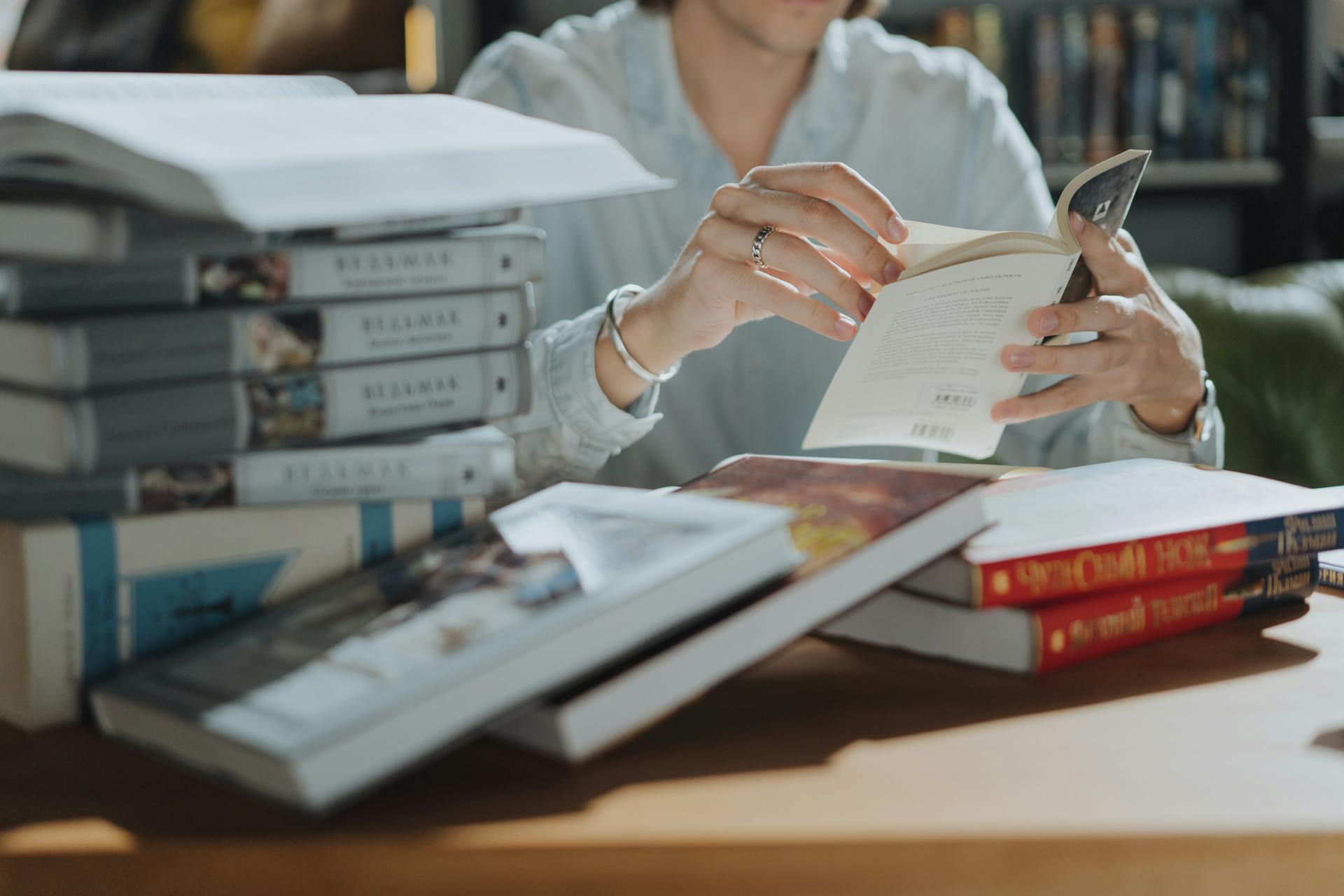 A young adult reading a book amidst a stack of books in a library, focusing on self-education and study.